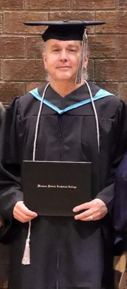 Picture of older man wearing cap and gown at graduation holding a diploma.